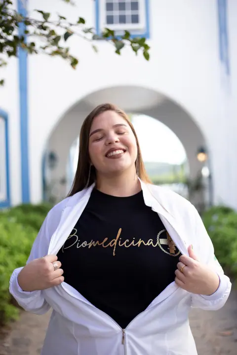 Formanda abrindo o jaleco e mostrando a camisa personalizada de Biomedicina