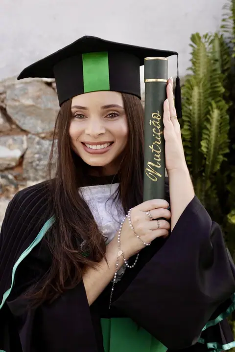 Formanda de Nutrição sorrindo com a beca e o canudo do curso