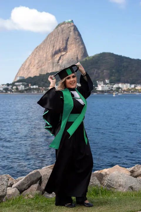 Formanda de beca com faixa verde em frente à baía e ao Pão de Açúcar