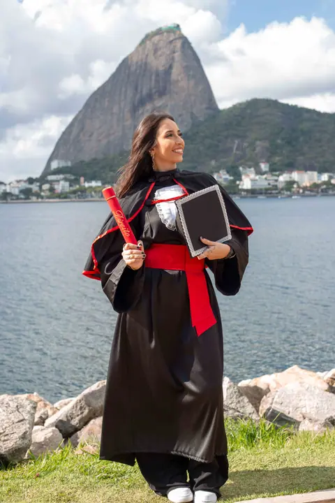 Formanda de beca com faixa vermelha segurando o canudo e o diploma